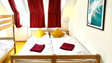 A room with two wooden beds, red curtains, a white radiator, and a framed picture on the wall.