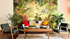 Una sala de estar con un sofá, dos sillones, una mesita de centro y un mural grande con temática tropical en la pared.