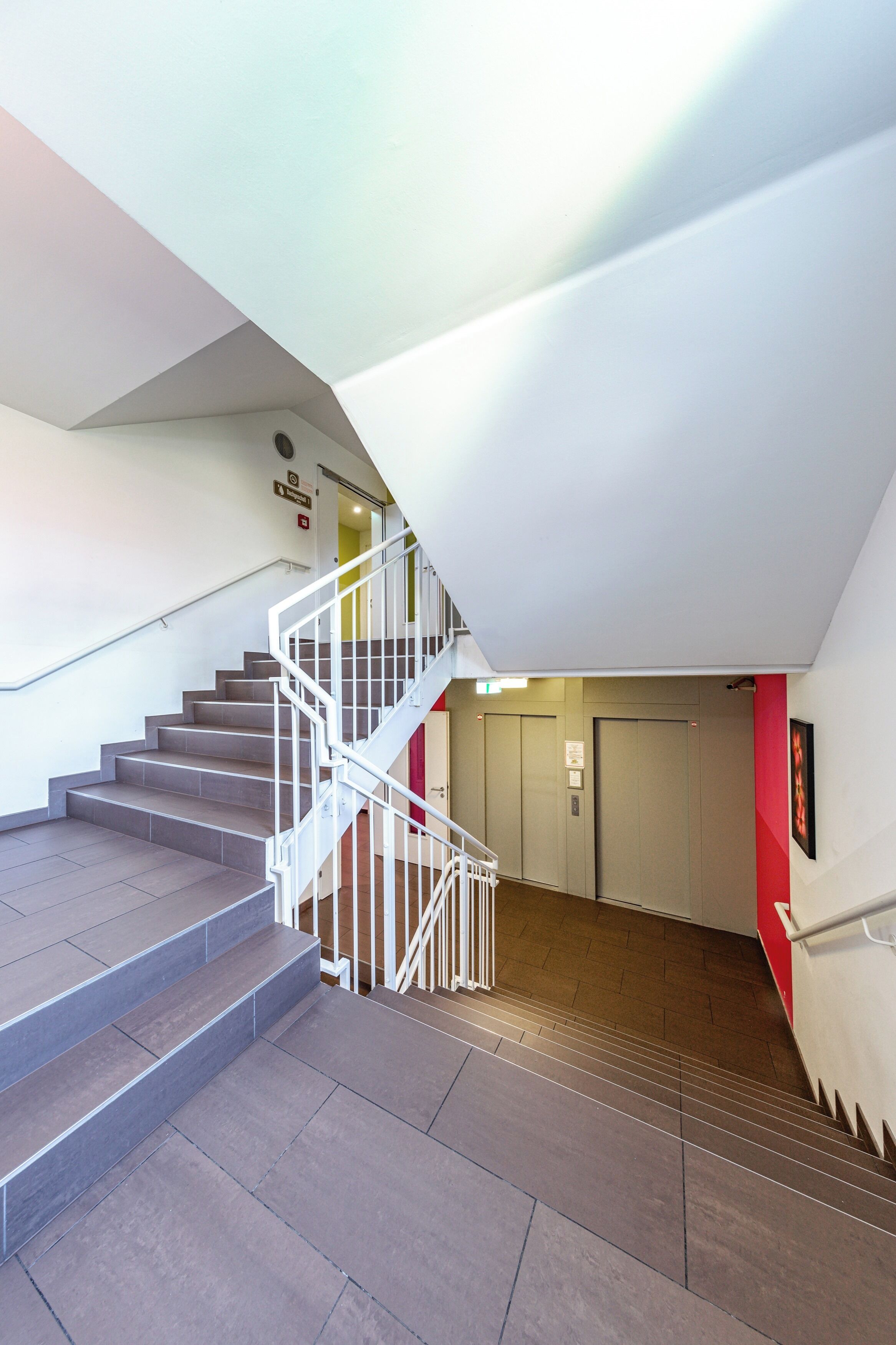 Un escalier moderne avec une rampe blanche, menant à un ascenseur.