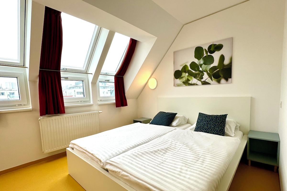 Quarto moderno com uma cama grande, duas mesas de cabeceira, um radiador e uma janela com cortinas.