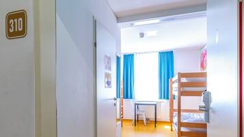 A corridor leading to a room with a bunk bed, a window with blue curtains, and a radiator.