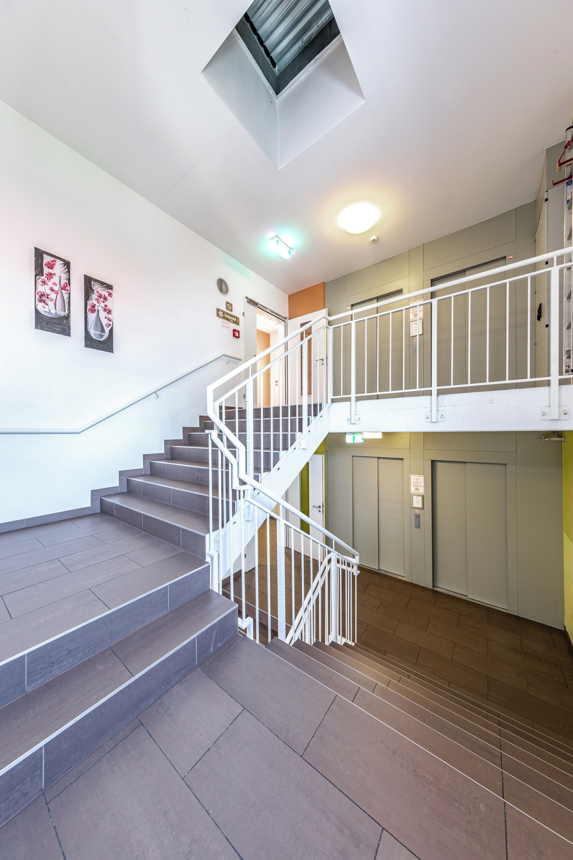 A staircase with a white railing leading to a second floor, a ceiling vent, and a door with a sign.