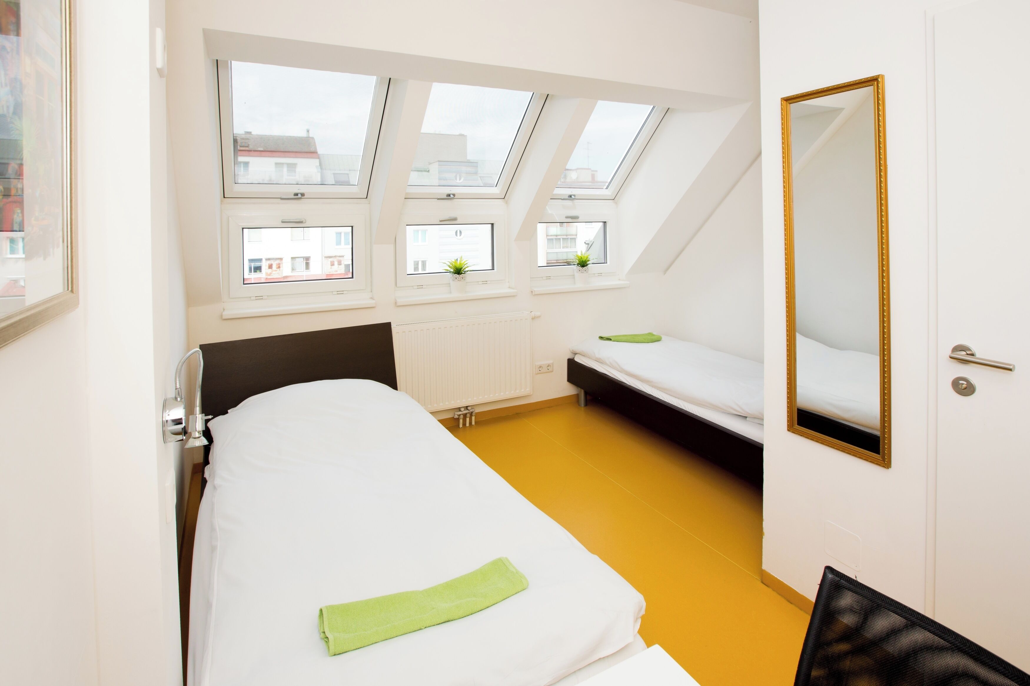 Quarto com cama, escrivaninha e janela com vista para edifícios.