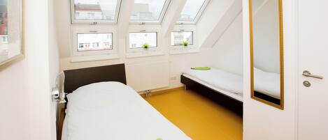 Quarto com cama, escrivaninha e janela com vista para edifícios.