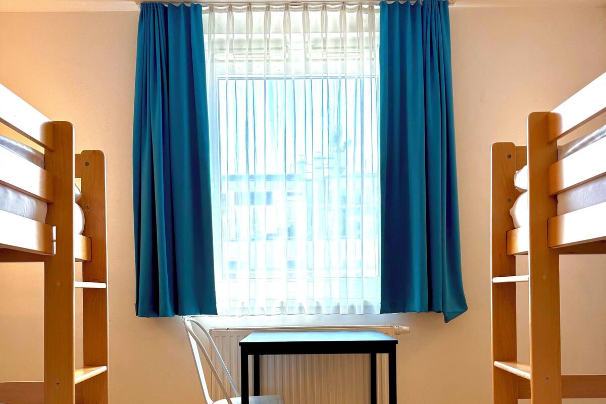 A dormitory room with bunk beds, a desk, and a chair.
