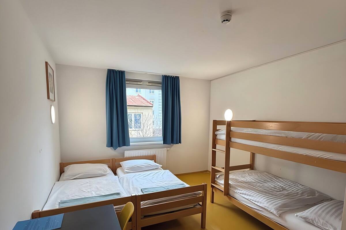 A dormitory room with two single beds, a desk, and a window with curtains.