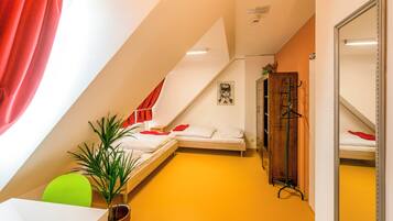 A compact, brightly colored room with two beds, a mirror, a green chair, and a potted plant.