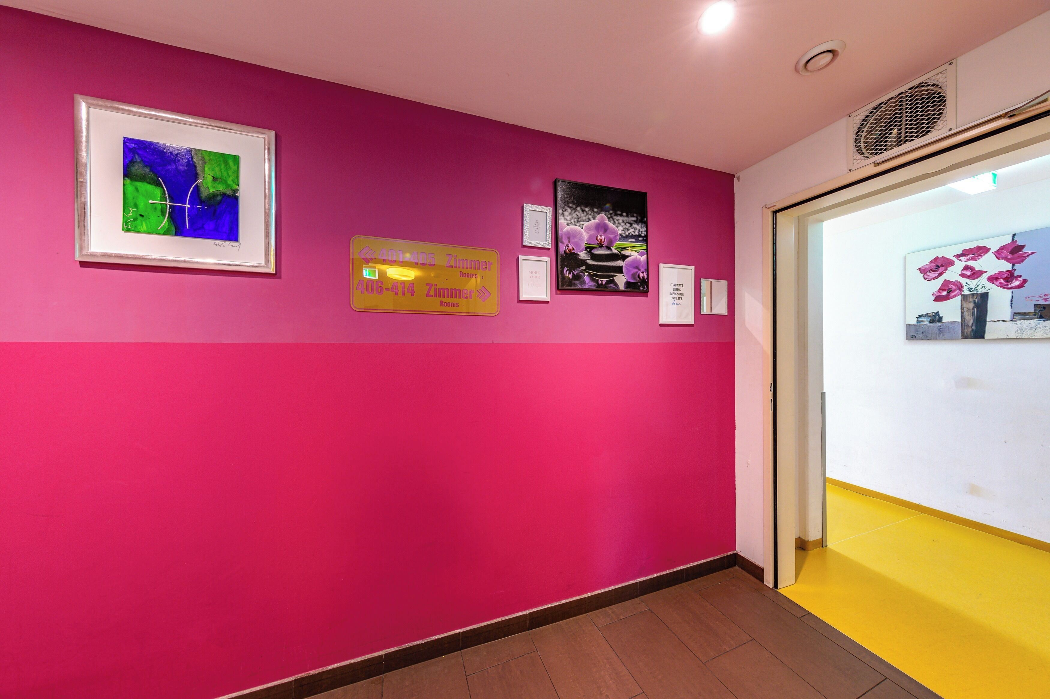 A hallway with a pink wall, framed artwork, and a yellow floor.