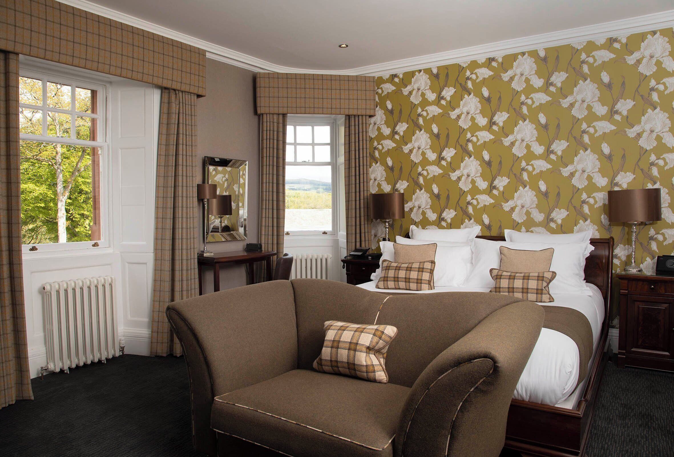 A bedroom with a large bed, a brown armchair, a dresser, and a window with curtains.