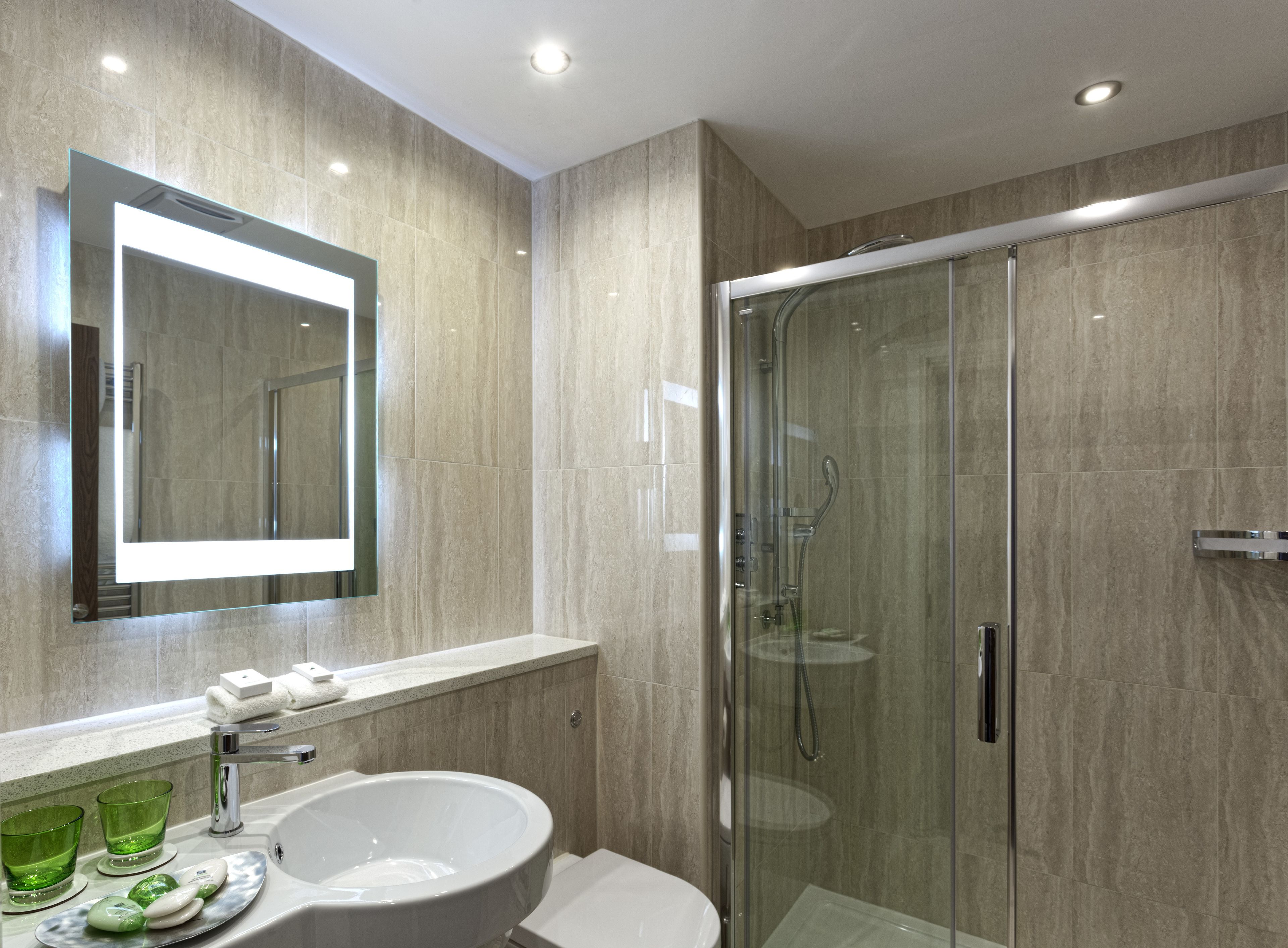 Une salle de bain moderne dotée d’une douche à parois de verre, d’un grand lavabo avec un miroir et d’un plan de toilette où sont posés les articles de toilette.