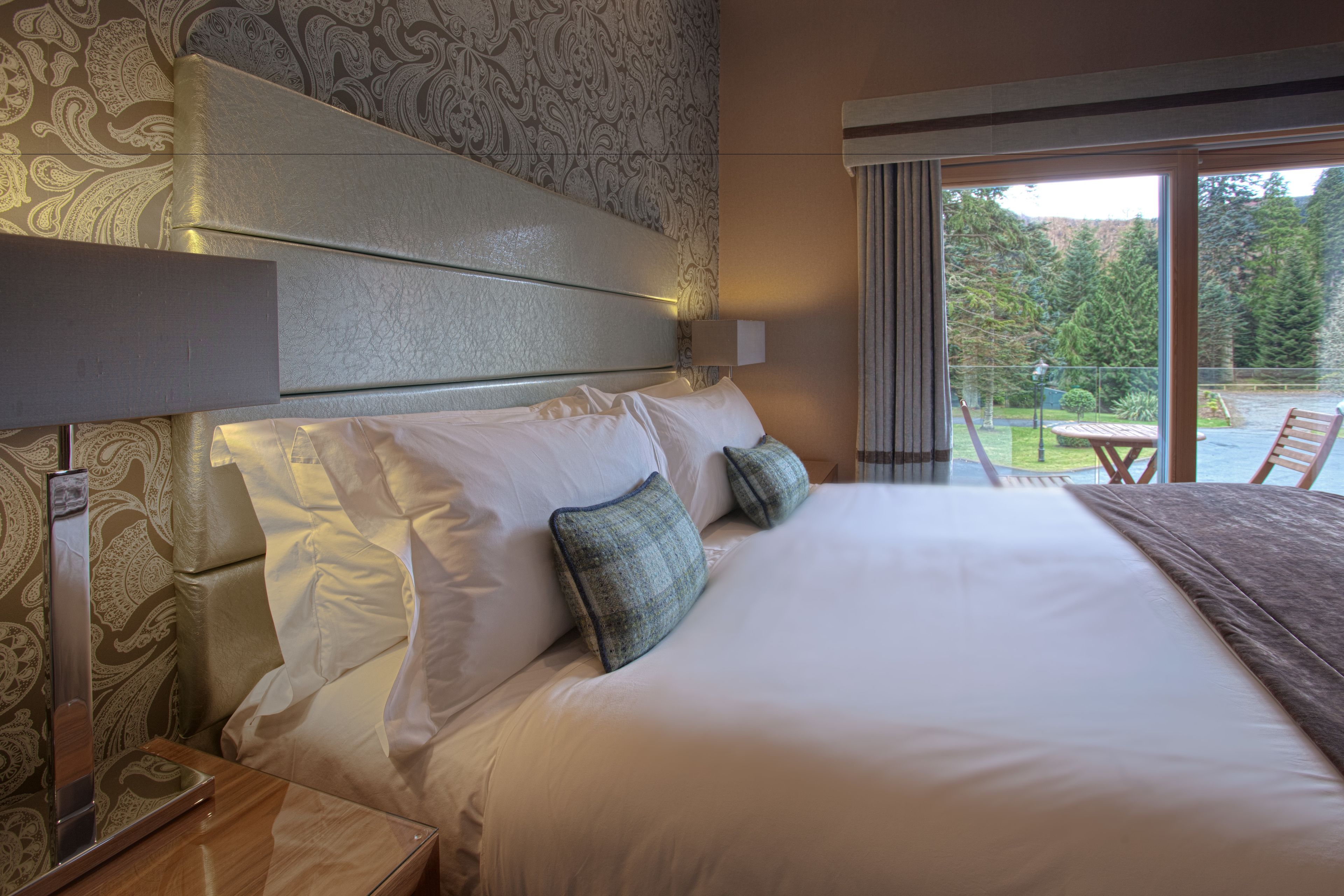 Ein Hotelzimmer mit einem großen Bett, einem Kopfteil, einem Nachttisch und Blick ins Freie.