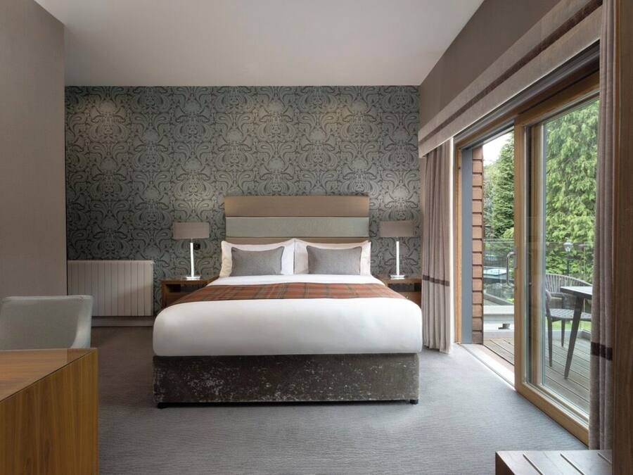 Une chambre d’hôtel moderne, dotée d’un grand lit, d’un bureau et offrant une vue sur l’extérieur grâce à une porte-fenêtre coulissante.