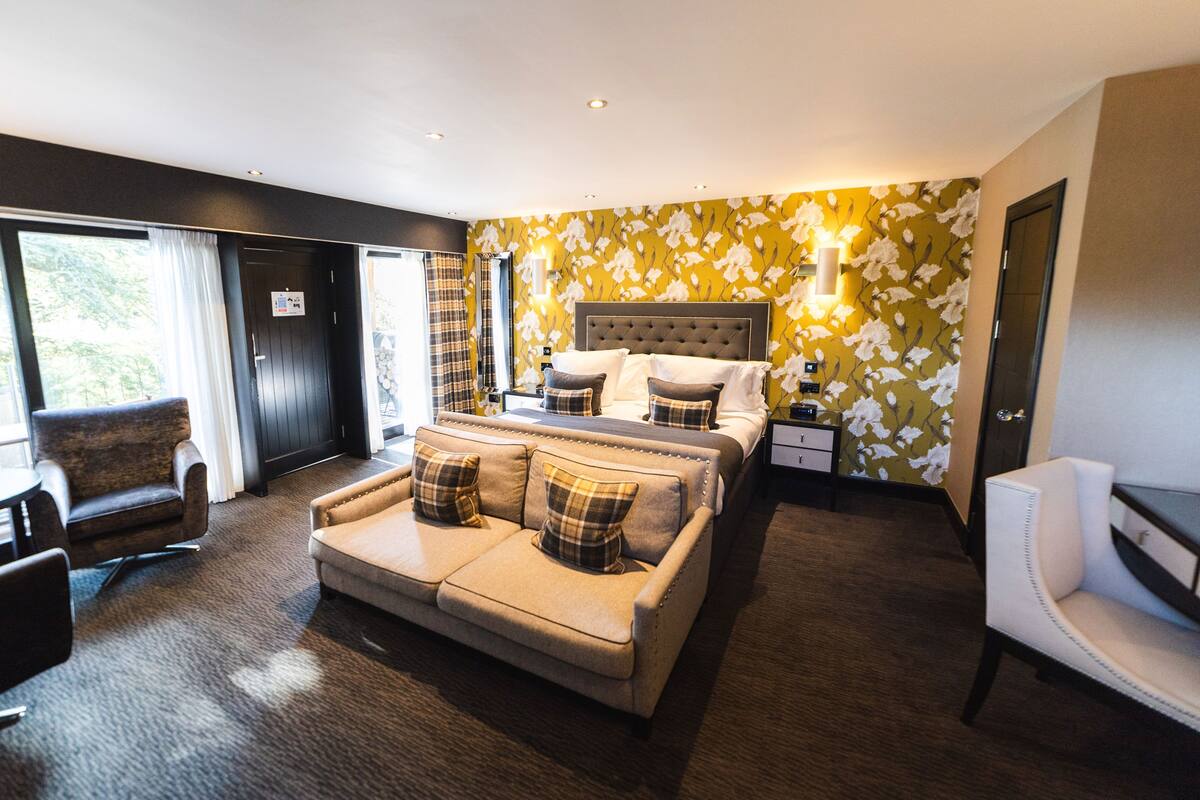 A modern hotel room with a large bed, a sofa, a chair, and a small table.