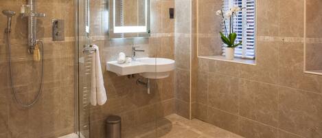 A modern bathroom with a glass-enclosed shower, a freestanding bathtub, a vanity with a mirror, and a window with blinds.