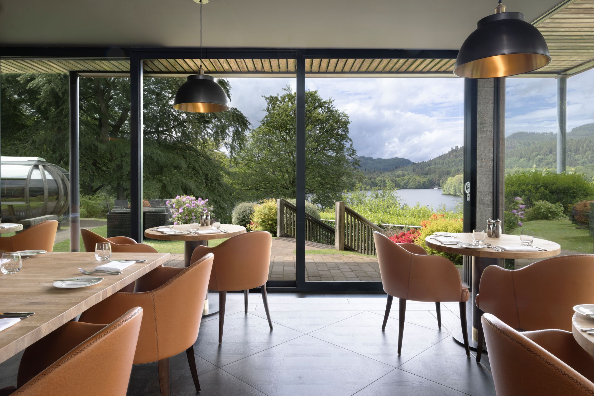Comedor con mesas y sillas, vista a un lago y un jardín.
