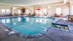An indoor swimming pool with lounge chairs and umbrellas, surrounded by walls with windows and informational posters. - MainStay Suites Rapid City (Rapid City)