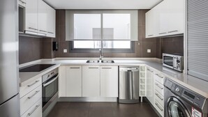Une cuisine moderne avec des meubles blancs, un four encastré, un lave-vaisselle et une machine à laver.