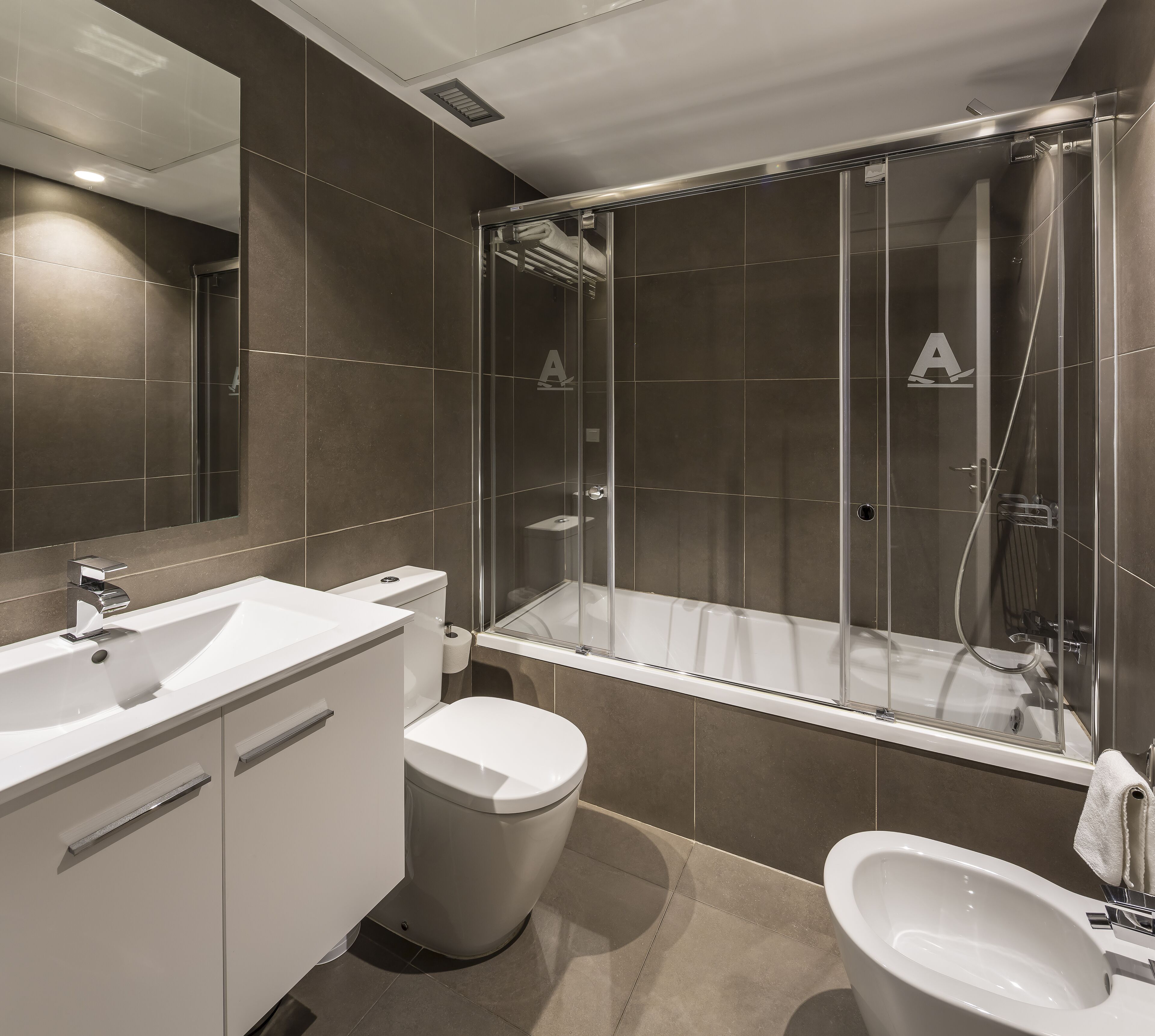 Un baño moderno con ducha de vidrio, un lavamanos blanco y un inodoro.