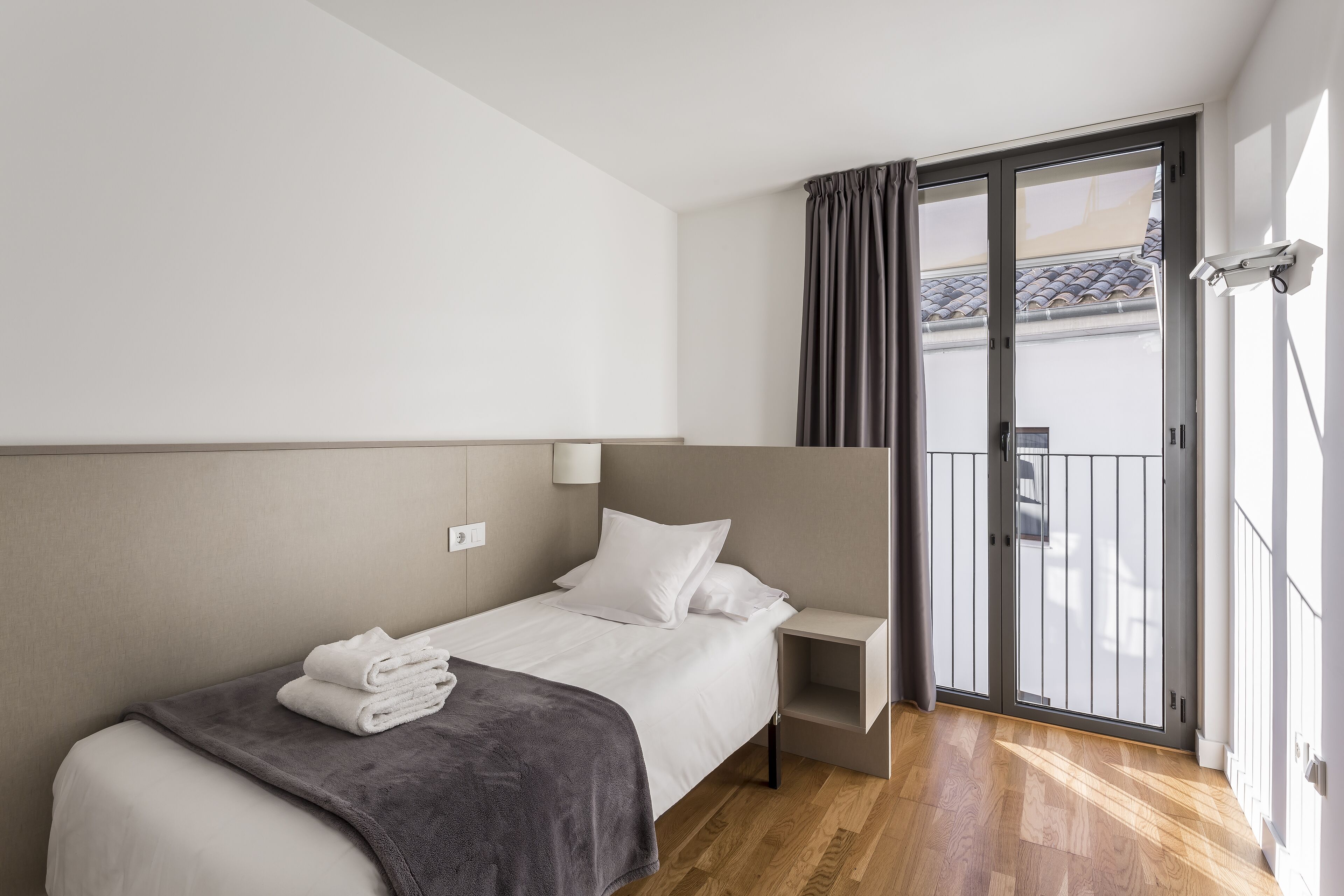 Habitación de hotel moderna con cama, mesita de noche, estante pequeño y puerta corrediza de vidrio a un balcón.
