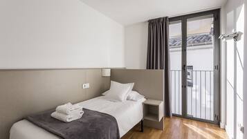 Habitación de hotel moderna con cama, mesita de noche, estante pequeño y puerta corrediza de vidrio a un balcón.