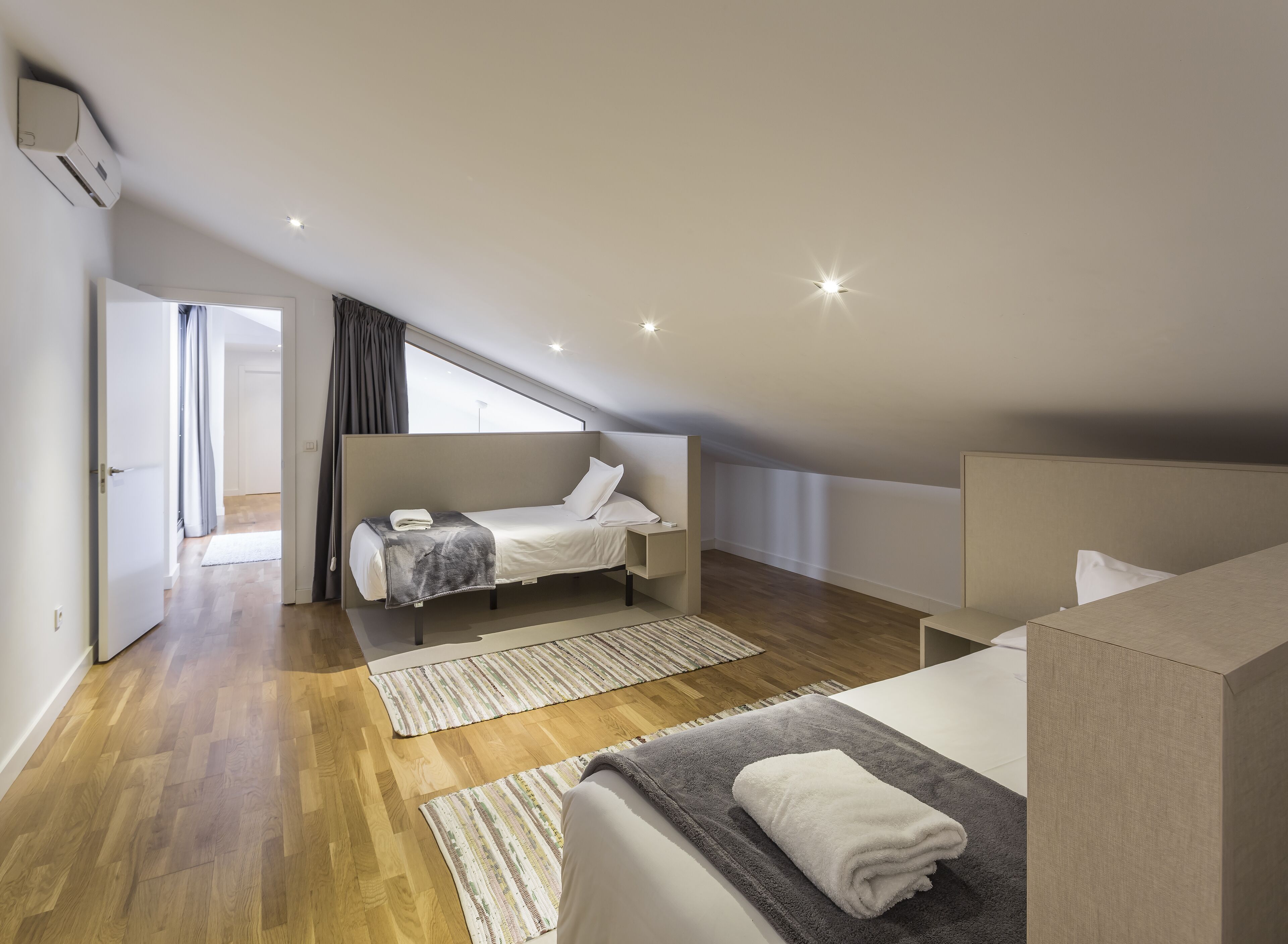 Un dormitorio moderno con cama tipo loft, una mesita de noche pequeña, un ventanal grande y suelo de madera.