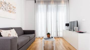 Una sala de estar moderna con un sofá gris, una mesa de centro blanca con una planta, un televisor de pantalla plana y un mueble blanco.