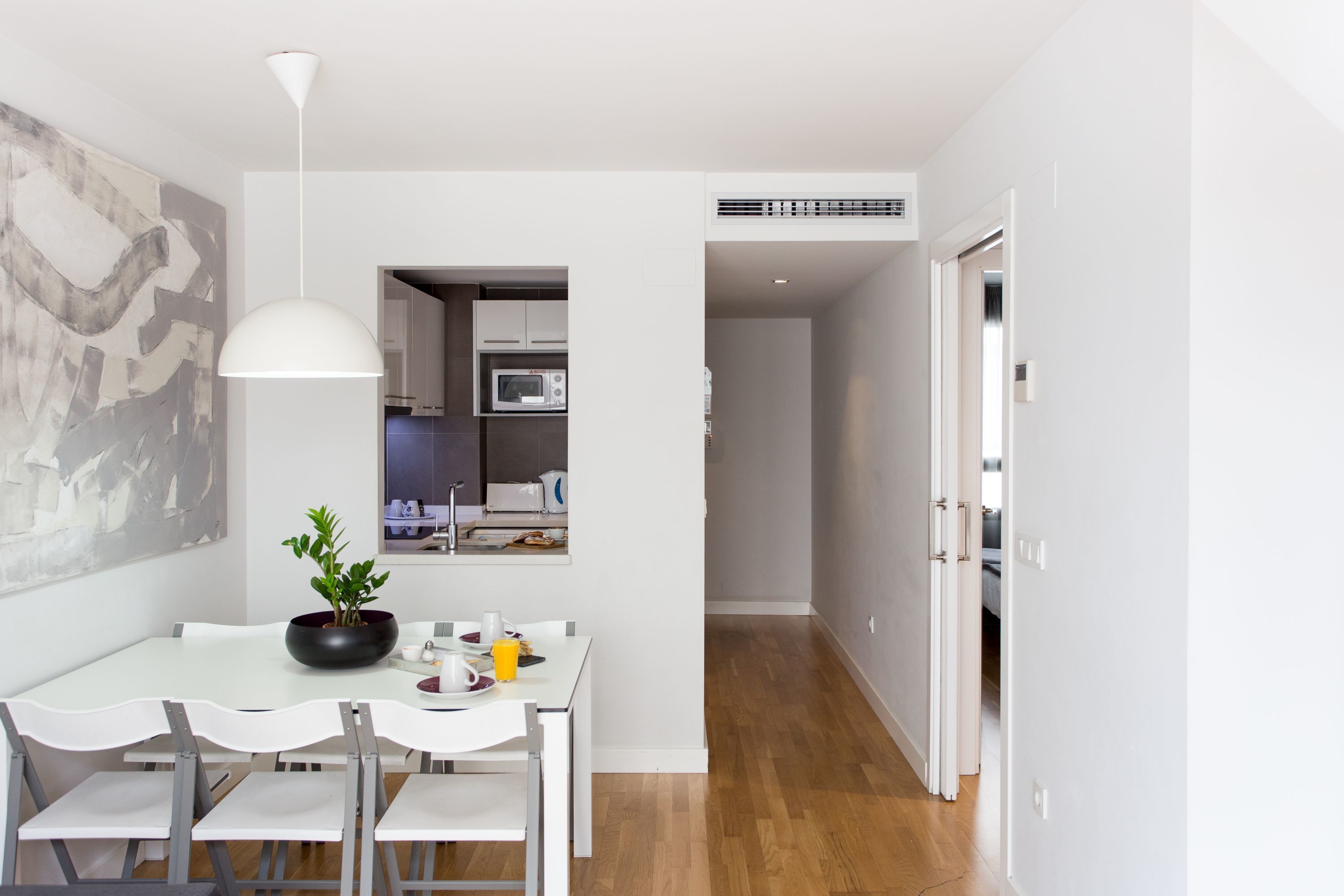 Een moderne keuken met witte kasten, een magnetron en een eethoek met een witte tafel en stoelen.