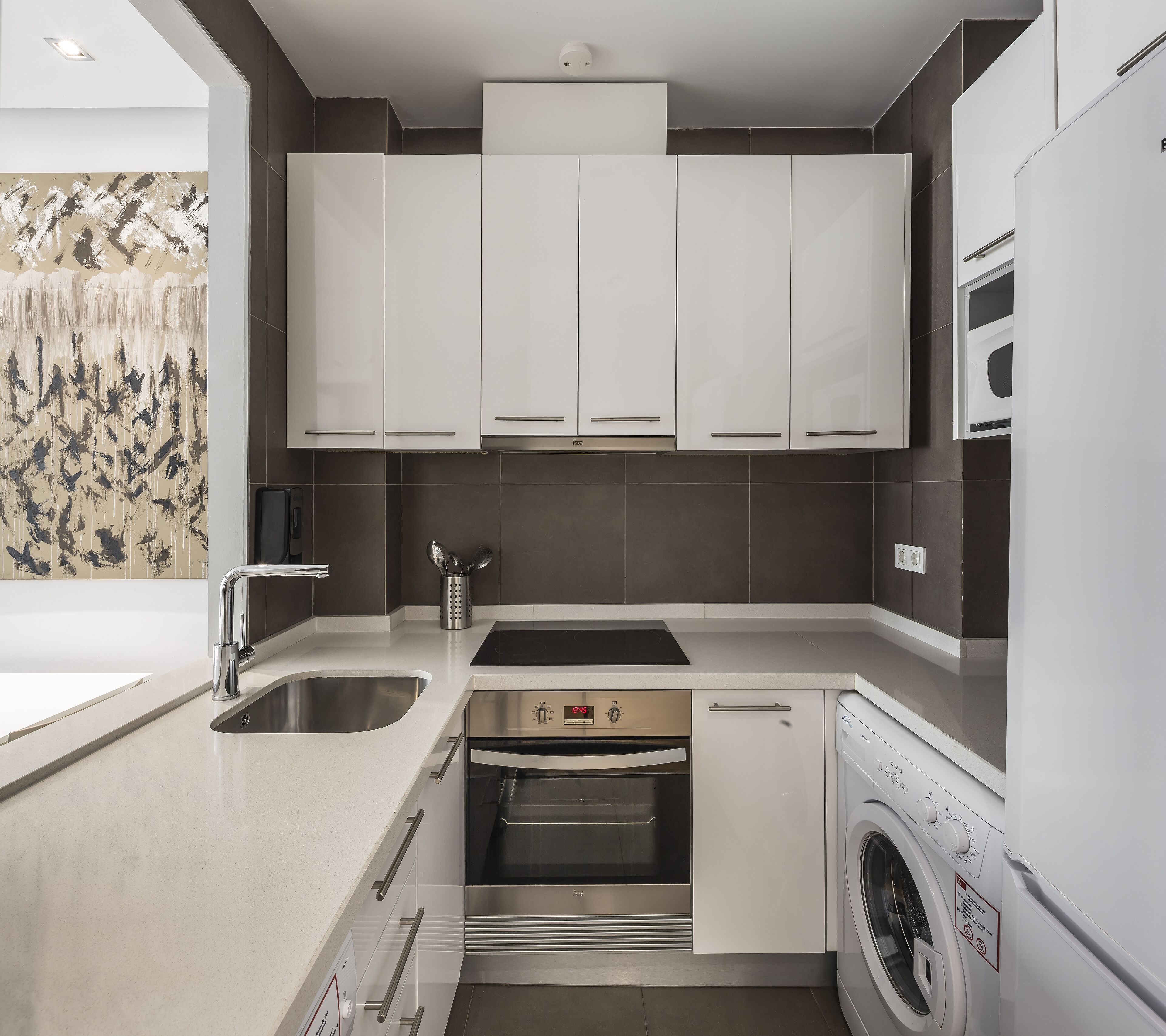 Una cucina moderna con mobili bianchi, elettrodomestici in acciaio inossidabile, forno integrato e lavatrice.
