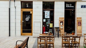 Un espace extérieur aménagé avec des tables et des chaises en bois, situé devant un bâtiment sur lequel on peut lire l’inscription « Bar et restaurant ».