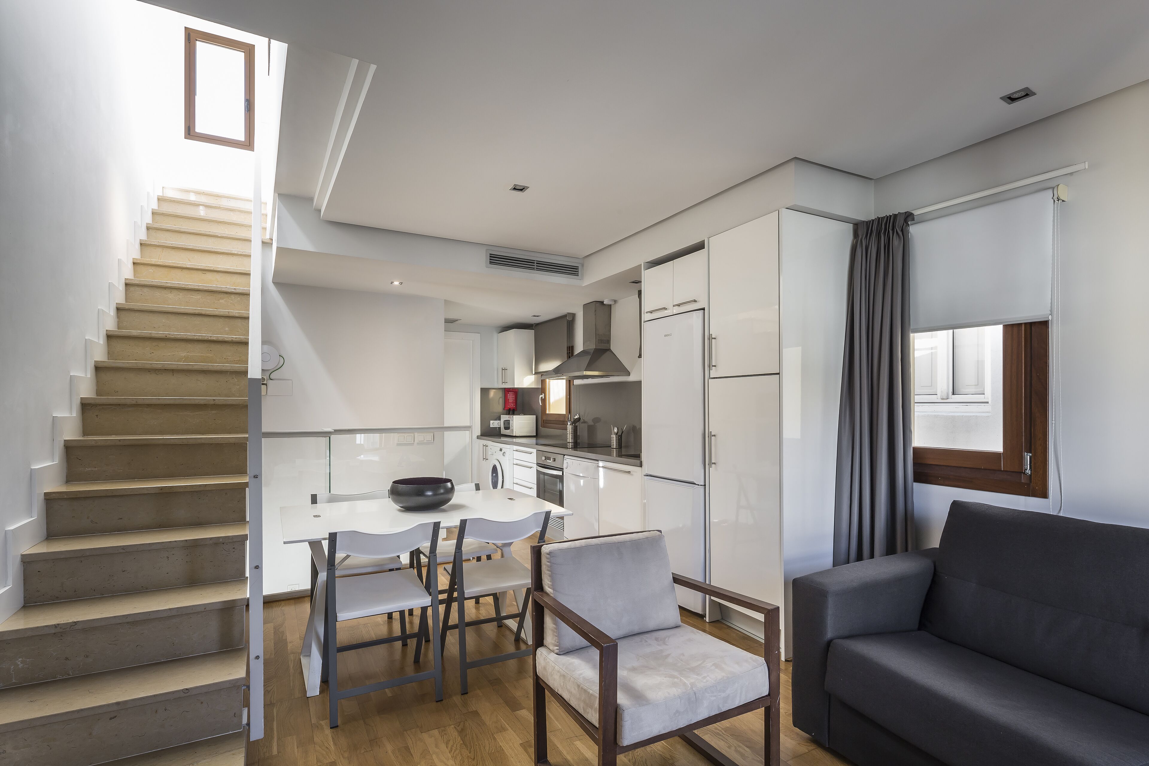 Une cuisine moderne avec des meubles blancs, un coin repas comprenant une table et des chaises, et un escalier.