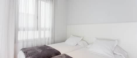 A bedroom with two beds, white bedding, and sheer curtains.