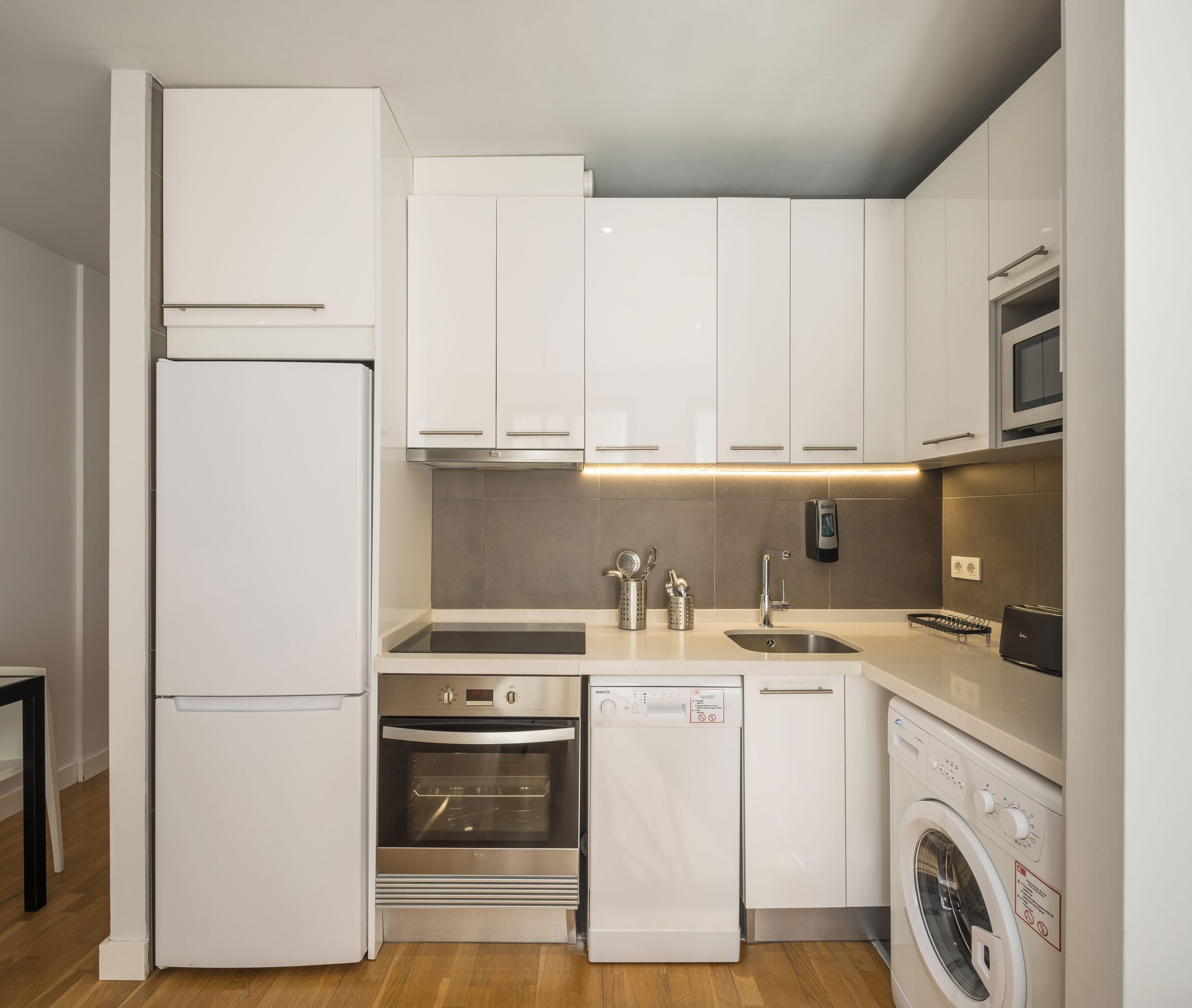 A compact kitchen with white cabinets, a built-in oven, a dishwasher, and a washing machine.