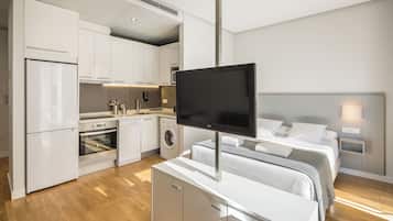 Une chambre d’hôtel moderne dotée d’une kitchenette, d’un lit avec une literie blanche et d’un téléviseur à écran plat fixé à un meuble.