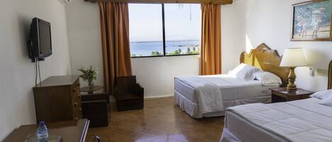 A hotel room with two beds, a TV, a ceiling fan, a window with curtains, a desk with a chair, and a water bottle on the desk.