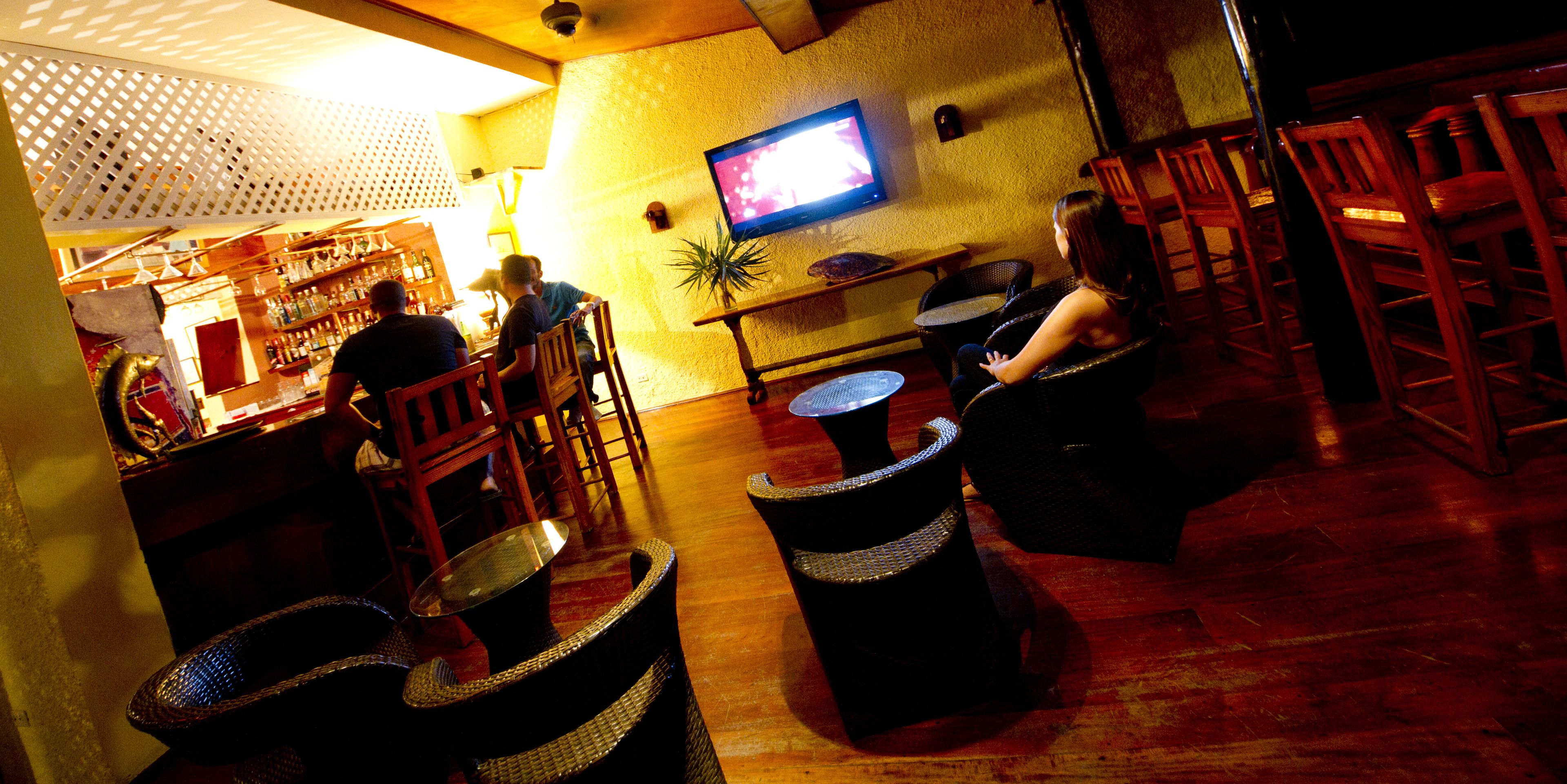 Eine Bar mit Holzhöckern, einem an der Wand befestigten Fernseher und einer Theke mit Flaschen.