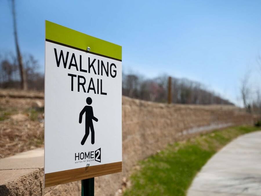 A sign for a walking trail with a figure of a person walking, and the text "HOME2 SUITES BY HILTON" below it.