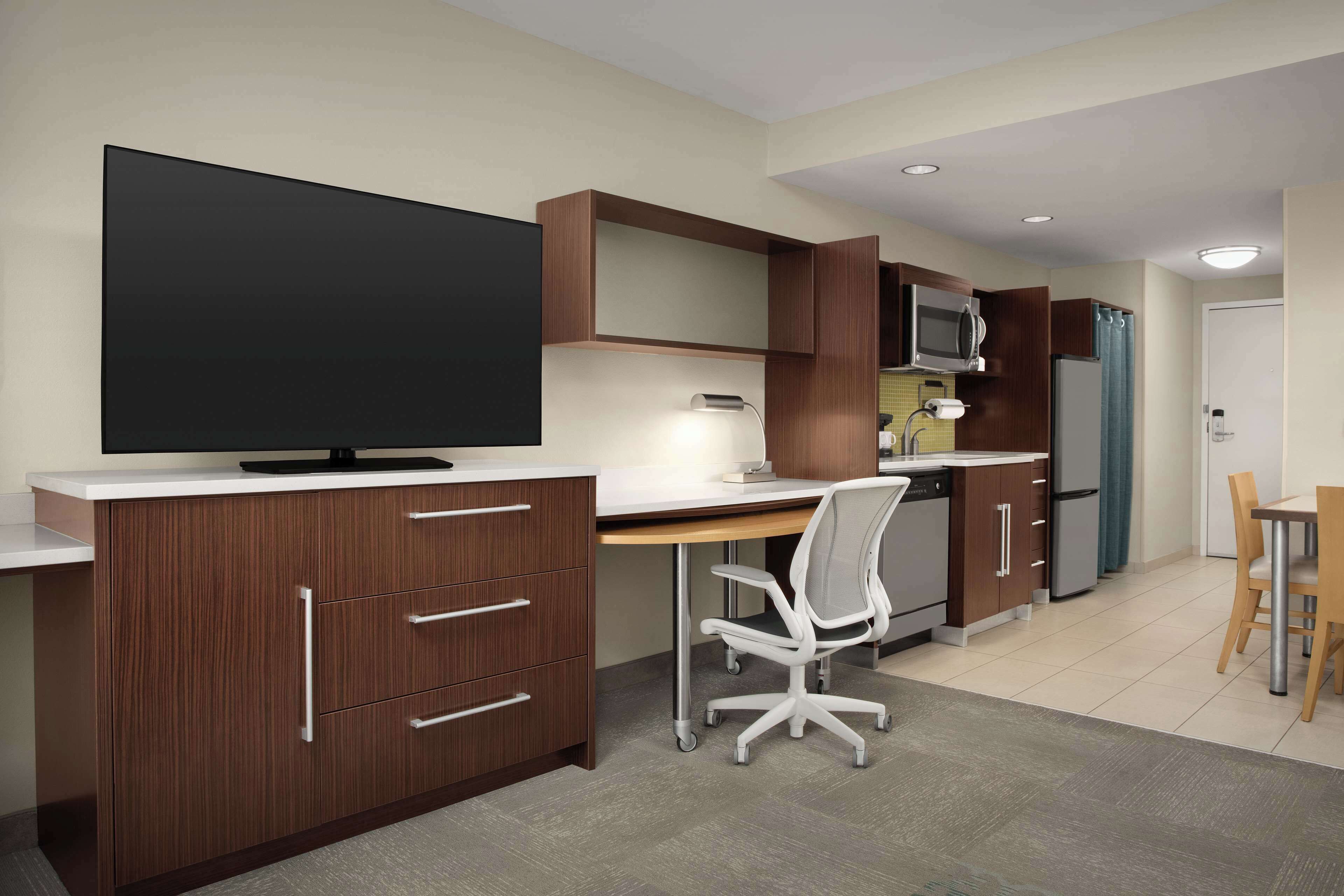 Una cocina moderna con televisor de pantalla plana, armarios de madera, una silla blanca y una mesa de comedor.