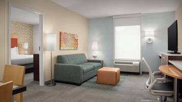 Quarto de hotel com cama, sofá, escrivaninha com cadeira, televisão e janela.