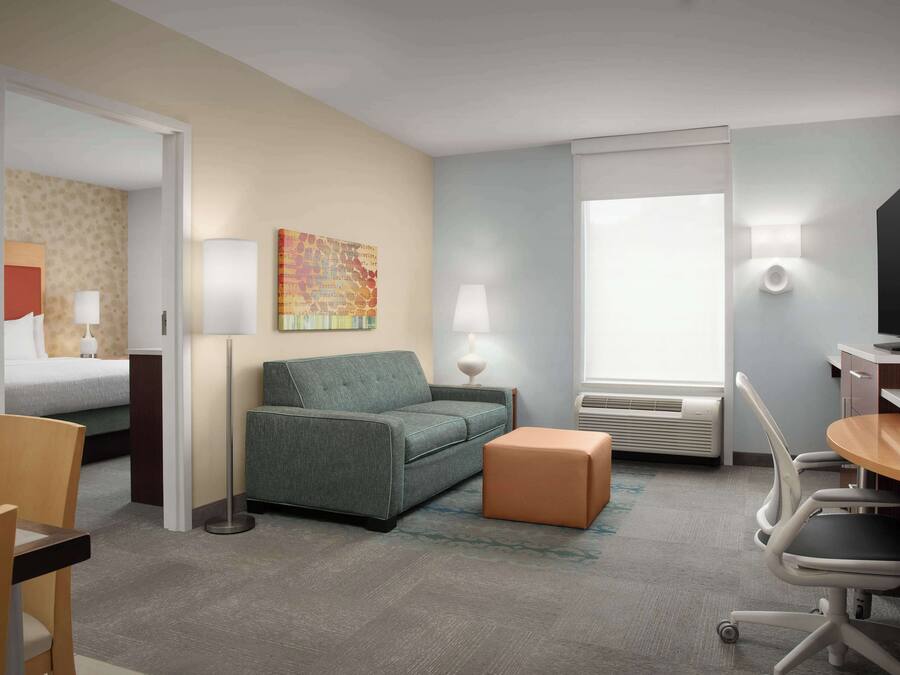 Quarto de hotel com cama, sofá, escrivaninha com cadeira, televisão e janela.