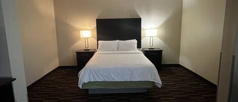Una habitación de hotel con una cama grande, dos mesitas de noche y un cabecero.