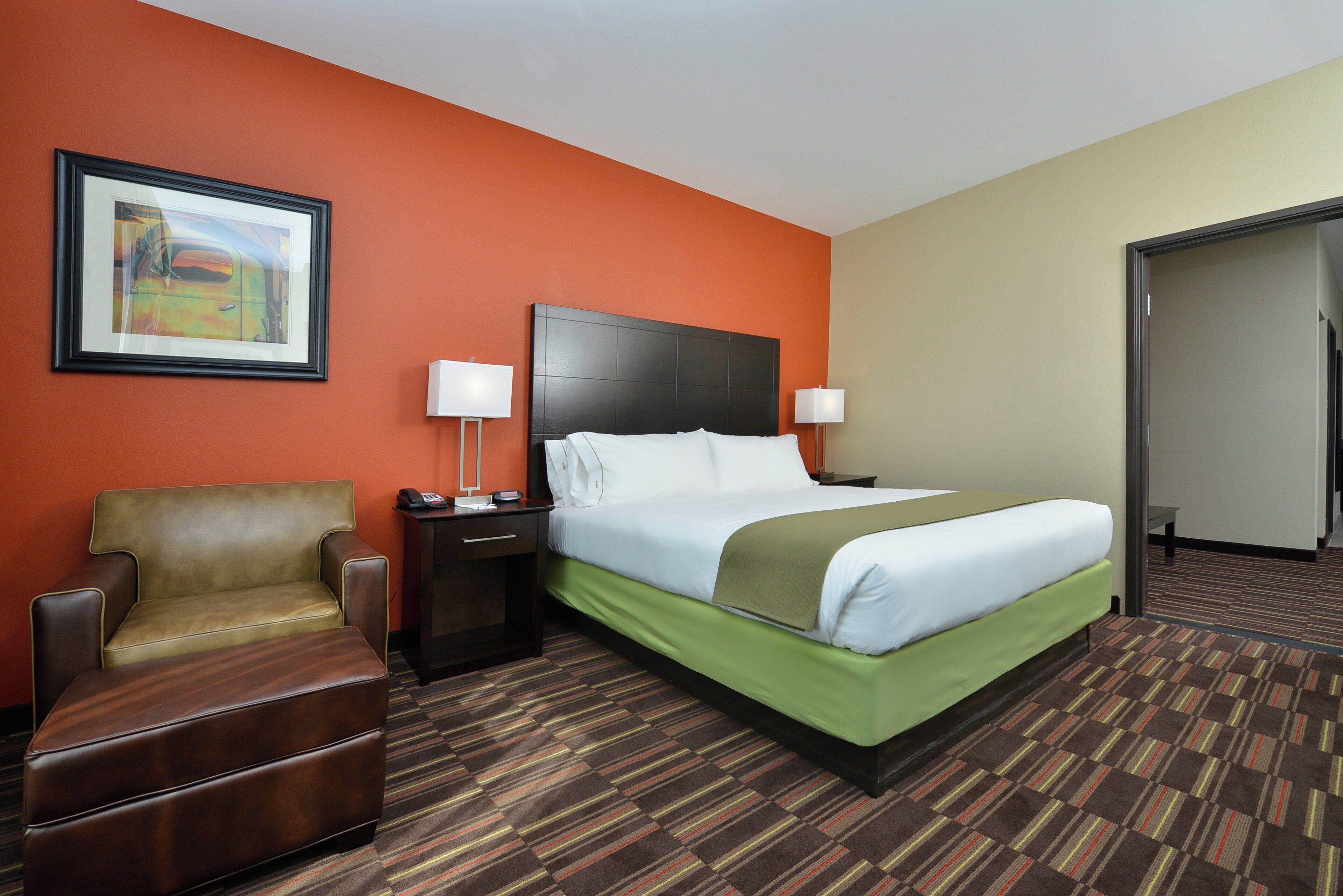 A hotel room with a bed, a chair, a nightstand, and a painting on the wall.
