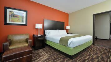 A hotel room with a bed, a chair, a nightstand, and a painting on the wall.