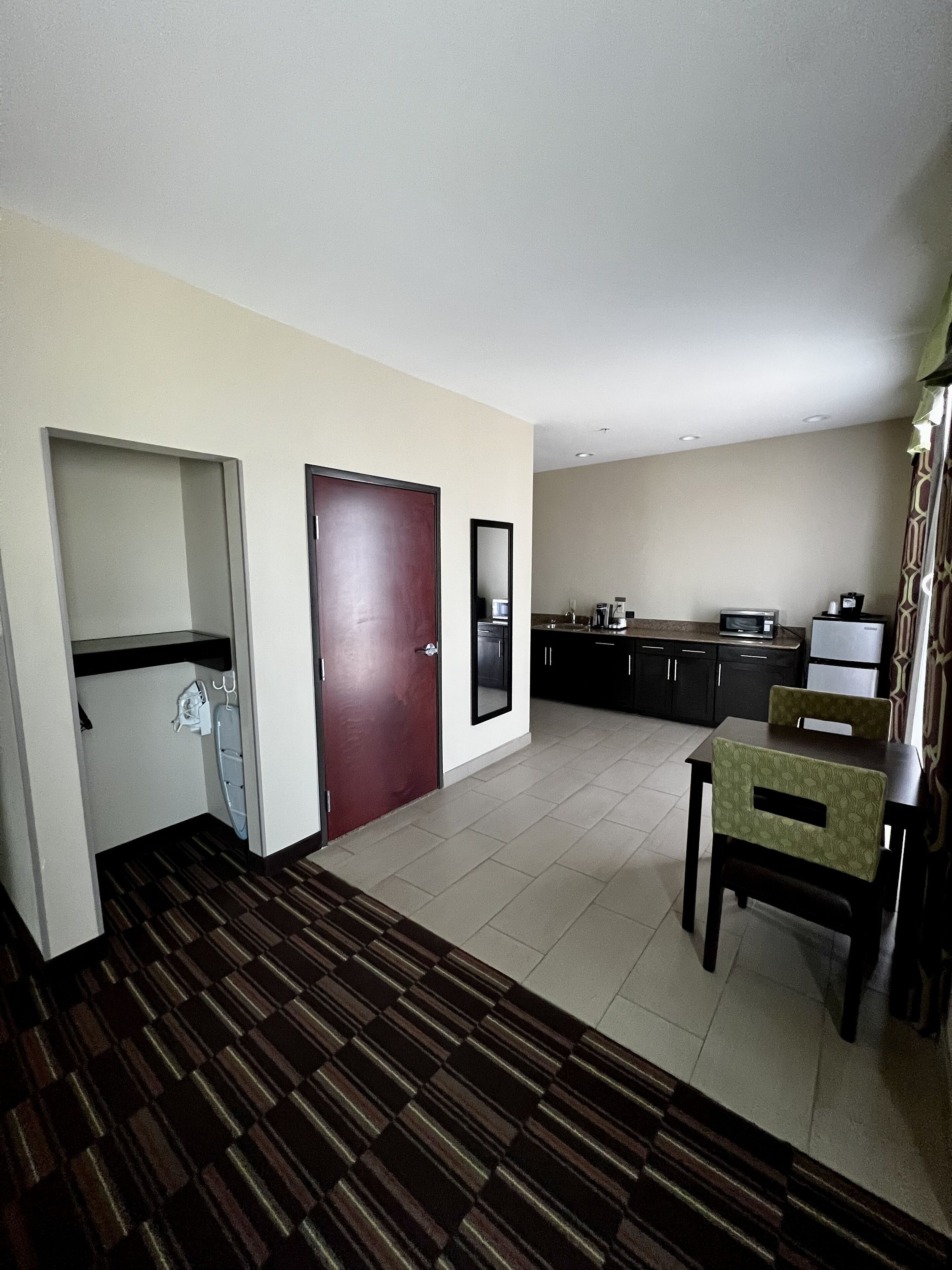 A hotel room with a kitchenette, a dining area with a table and chairs, and a patterned carpet.