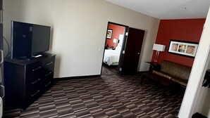 A hotel room with a television, a sofa, a patterned carpet, and a red accent wall. - Holiday Inn Express Hotel & Suites Alva by IHG (Alva)