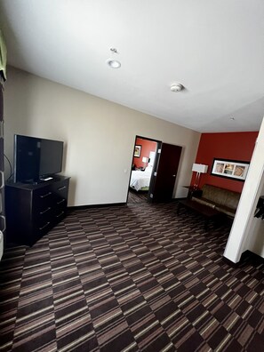 Une chambre d’hôtel équipée d’une télévision, d’un canapé, d’une moquette à motifs et d’un mur d’accent rouge.