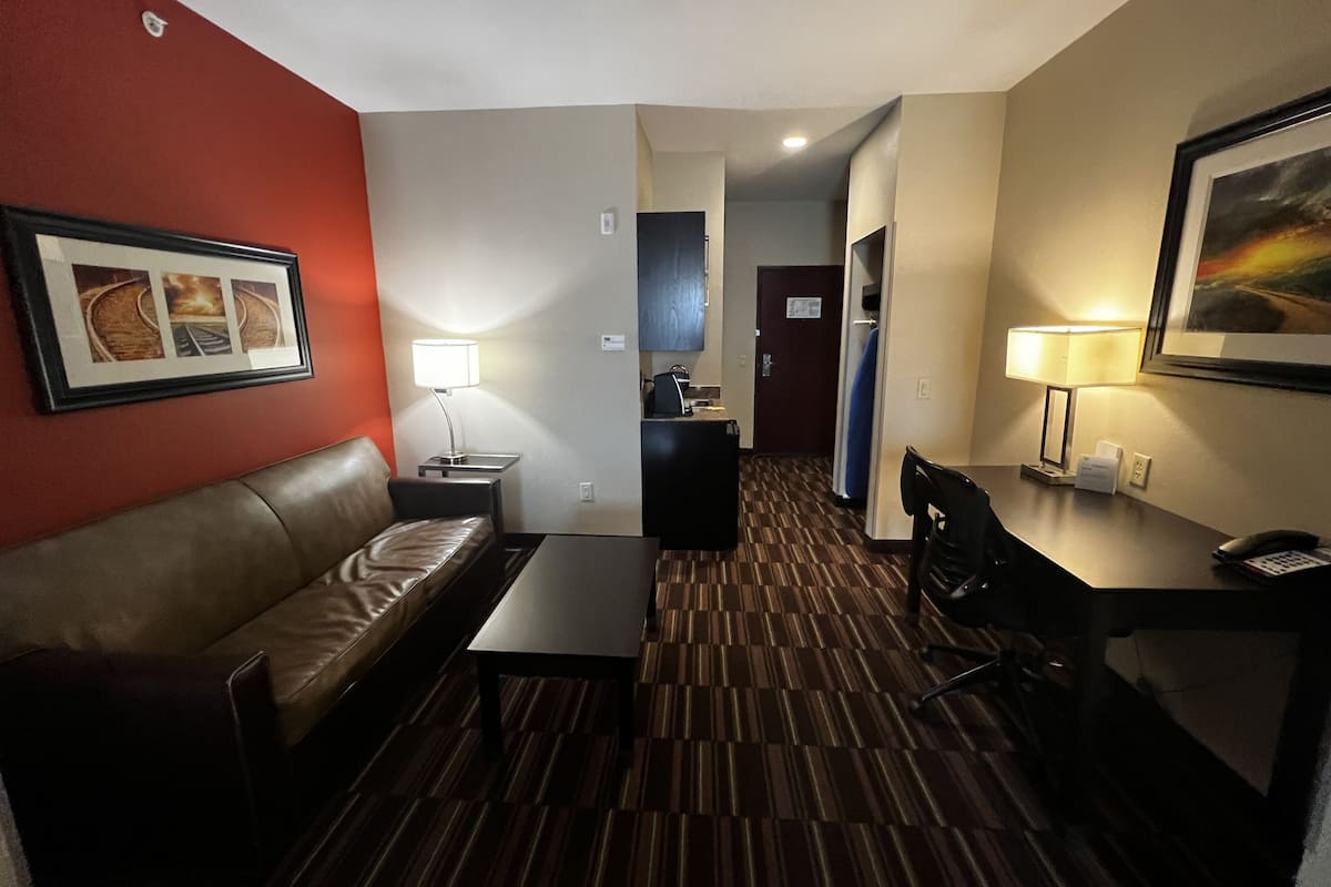 A hotel room with a leather sofa, a small table, a desk with a lamp, and a framed picture on the wall.