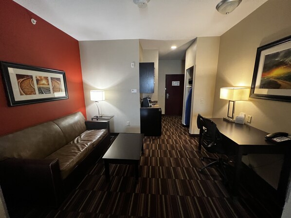 Une chambre d’hôtel avec un canapé en cuir, une petite table, un bureau avec une lampe et un tableau encadré au mur.