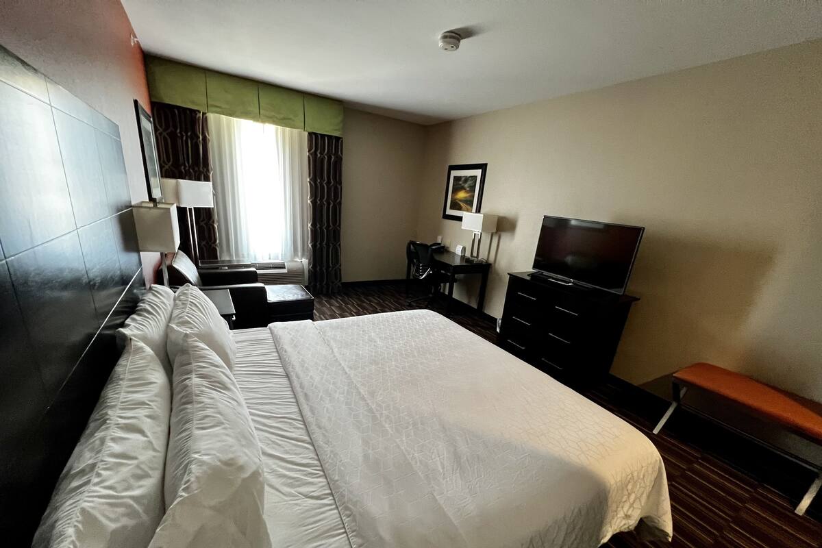 A hotel room with a large bed, a desk, a television, and a window with curtains.