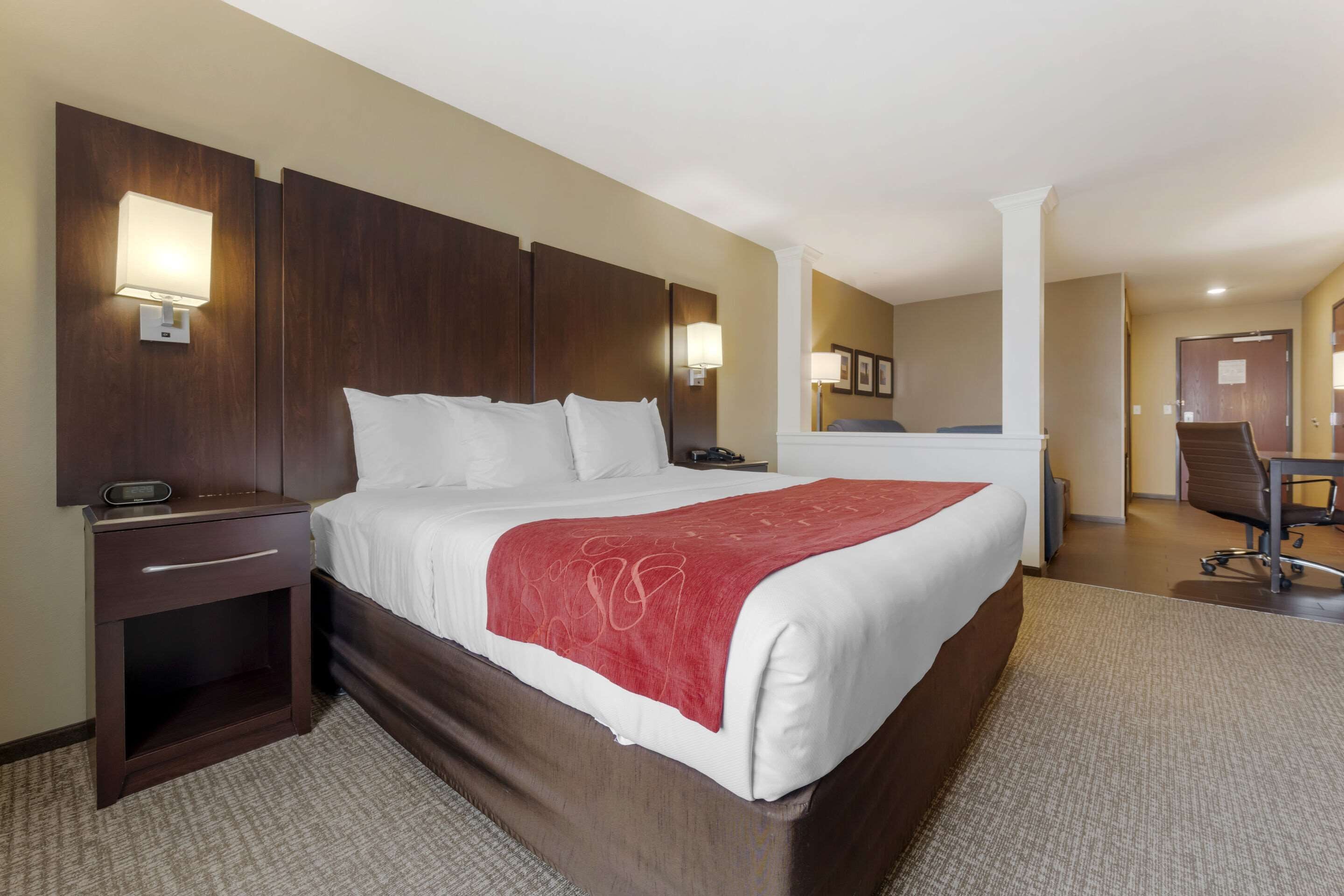 A hotel room with a large bed, a nightstand, a desk, and a chair.