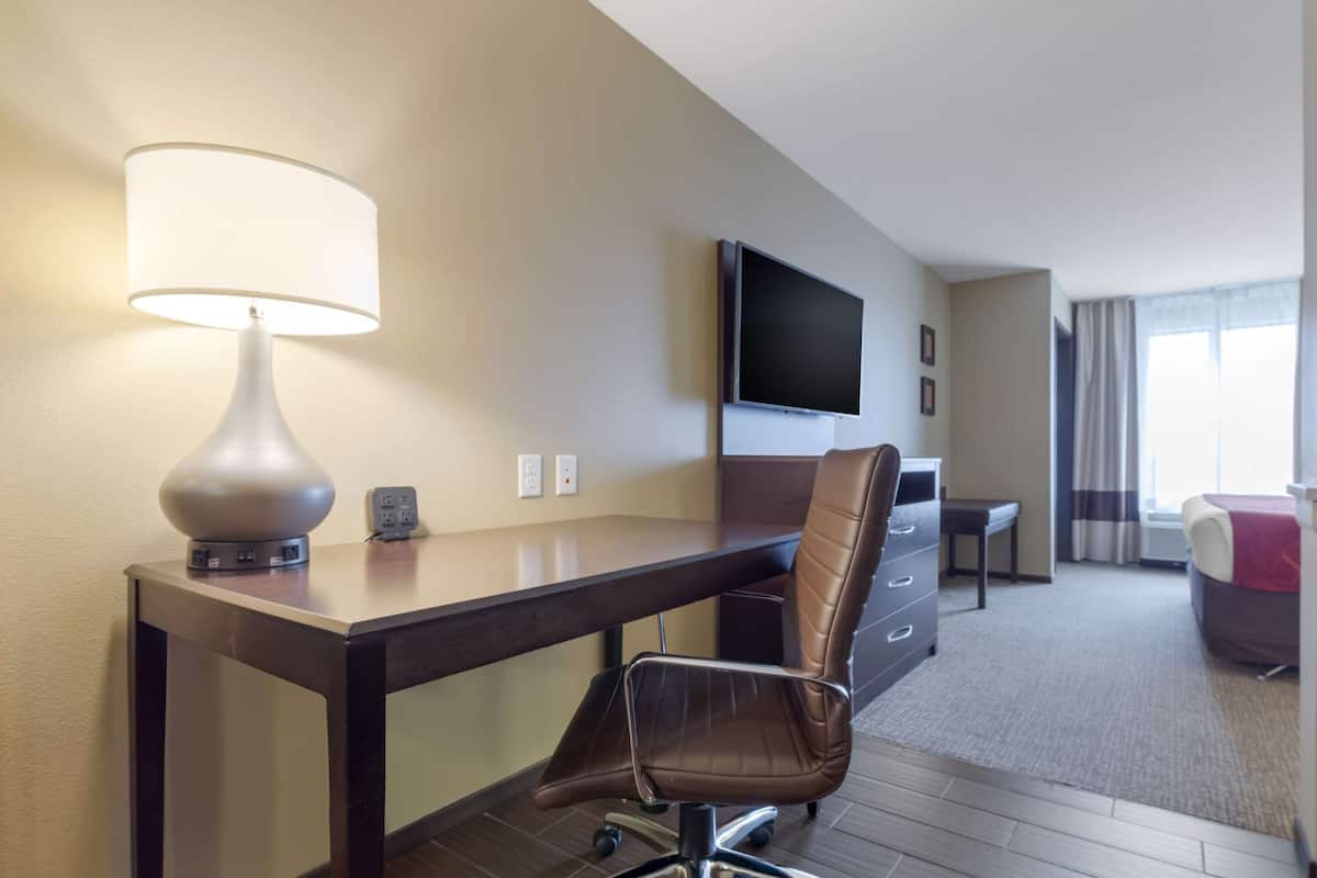 A hotel room with a desk, chair, lamp, TV, and a bed.